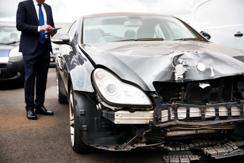 Male insurance loss adjuster with digital tablet inspecting damaged car